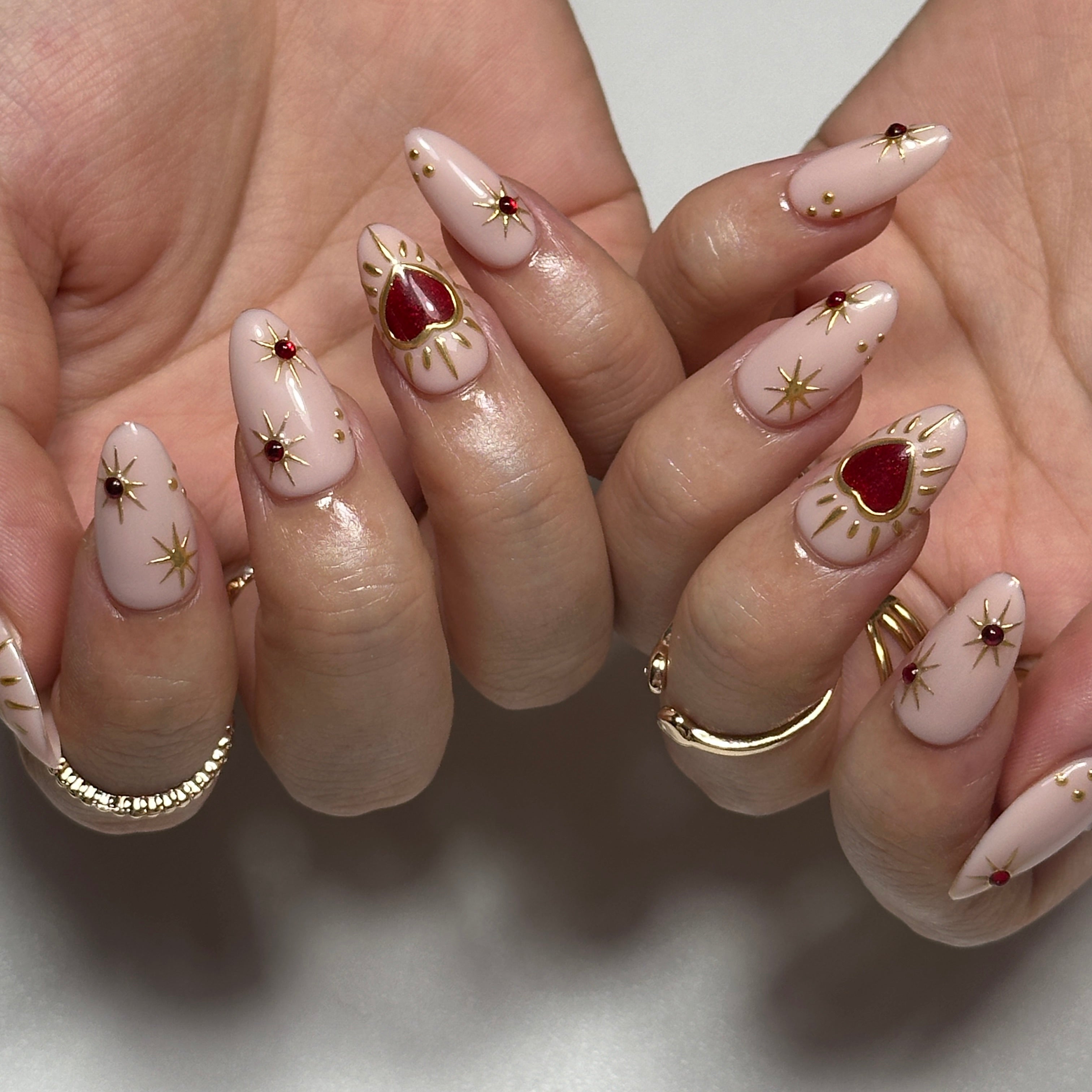 Close-up of hands with decorative nails featuring red and gold designs on a neutral background
