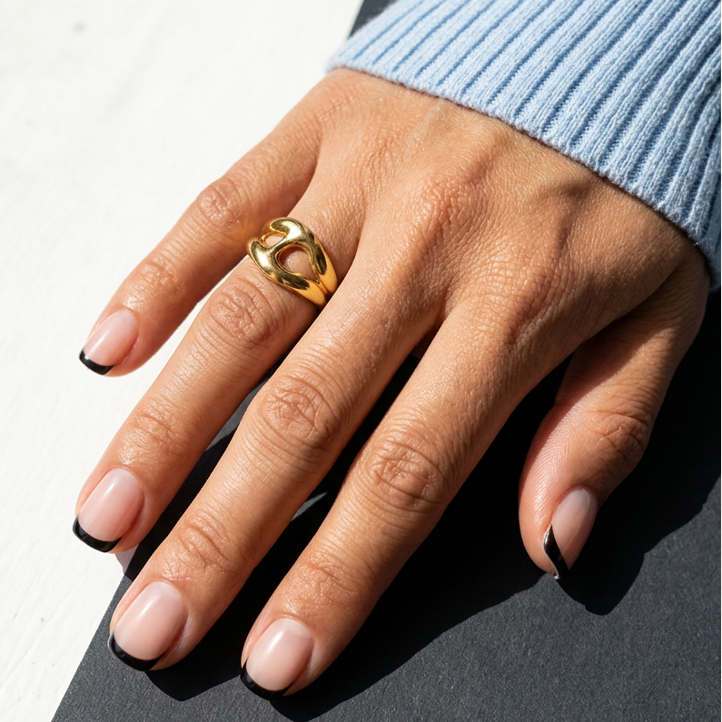 Hand wearing a gold ring on a neutral background