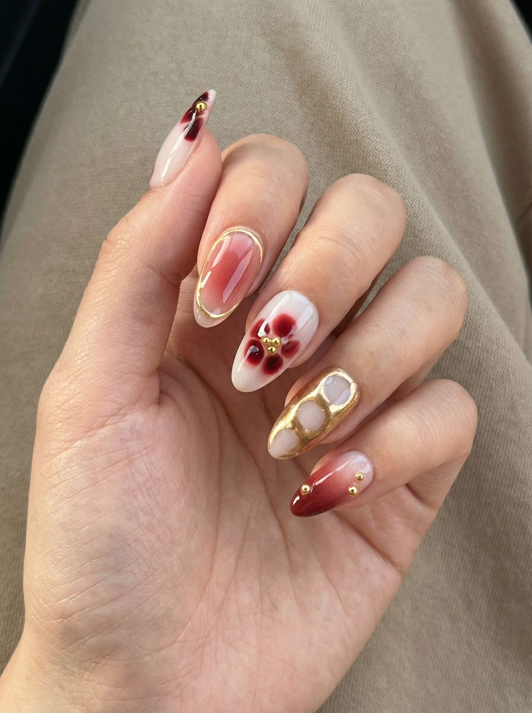 Hand with intricately designed nails featuring gold accents and red patterns.