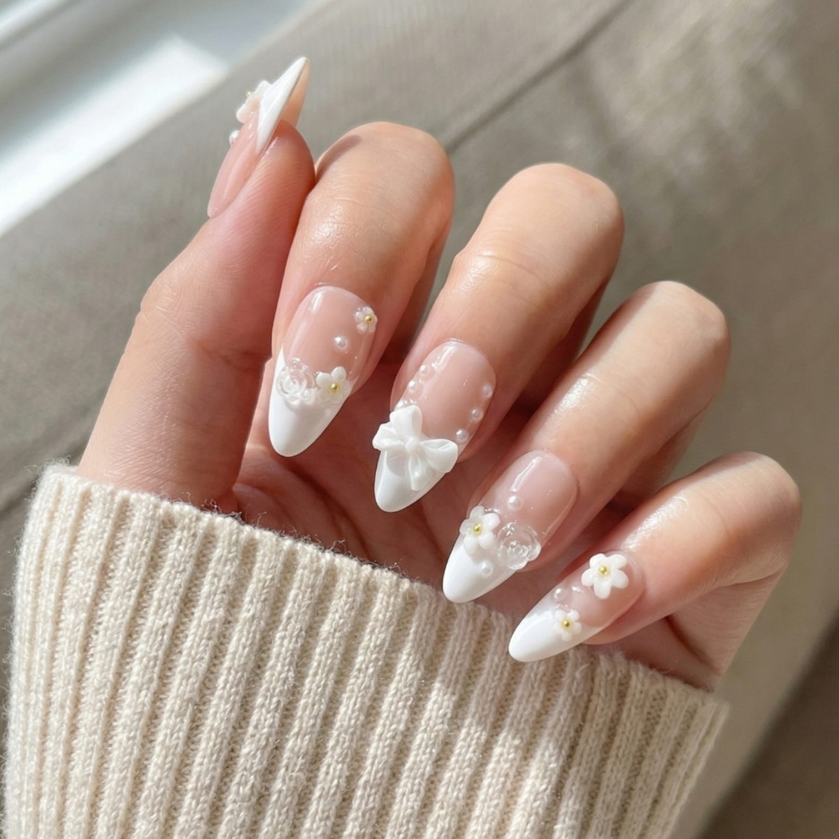Hand with almond-shaped nails featuring white floral designs, wearing a beige sweater.