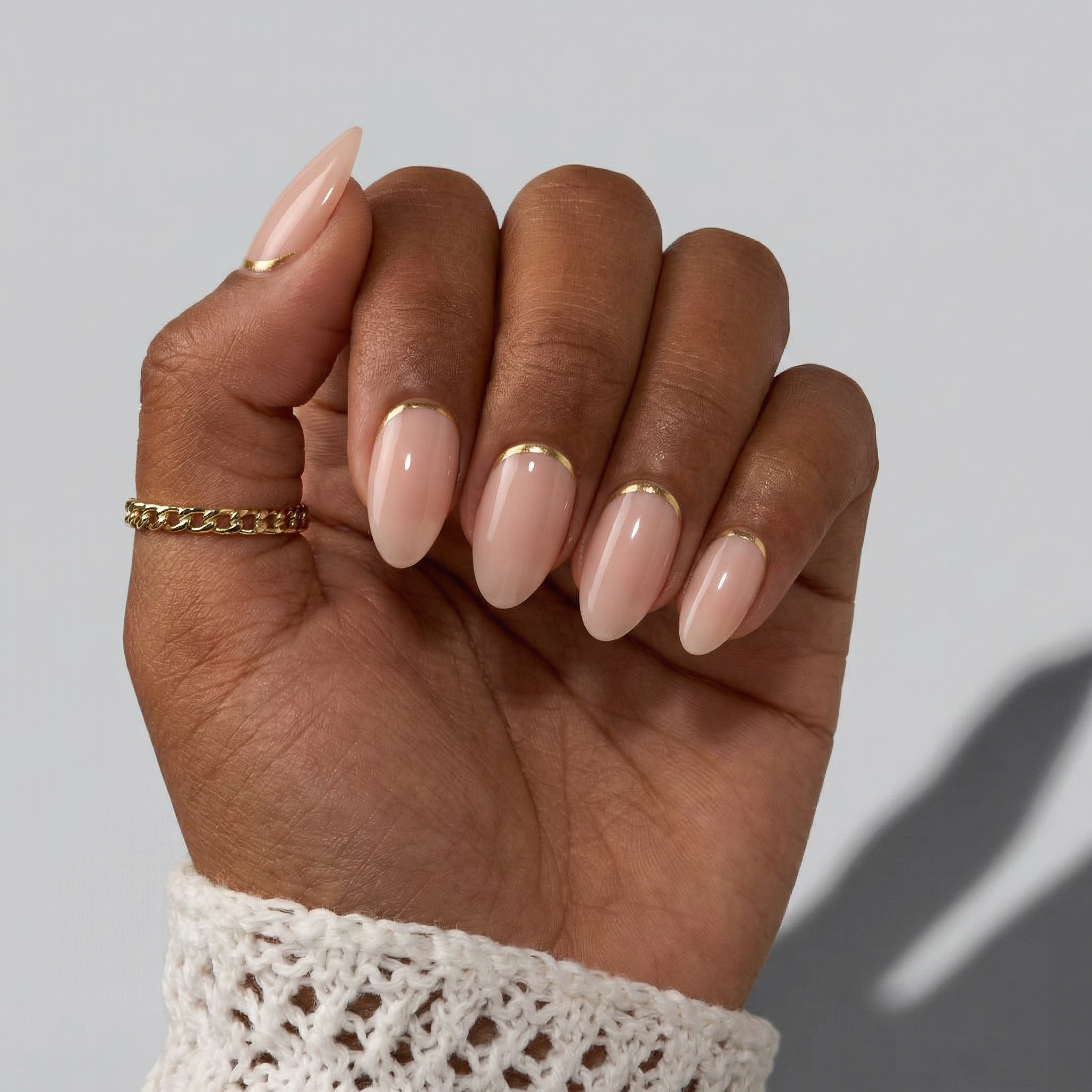 Hand with beige nail polish and gold accents on a neutral background