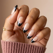 Hand with black and white nail design holding a pink sweater sleeve against a beige background