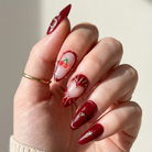 Hand with red nail art holding a white object against a neutral background