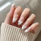 Hand with almond-shaped nails featuring white floral designs, wearing a beige sweater.