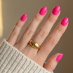 Hand with pink nails and a gold ring against a neutral background
