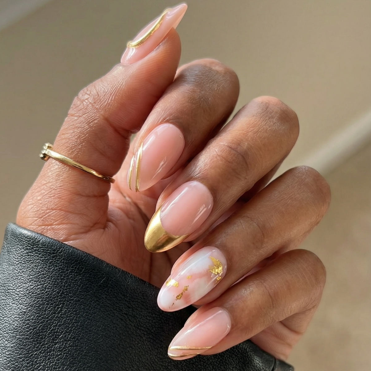 Hand with pink nail polish and gold accents wearing a black sleeve.