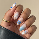 Hand with intricately designed nails featuring flowers and dots on a beige background